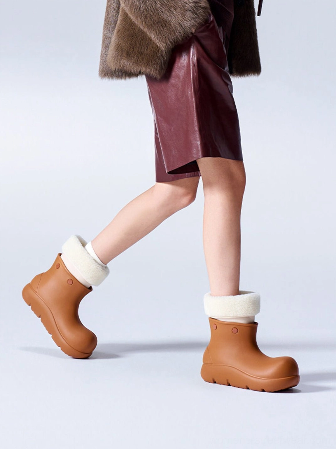 Model walking in brown fur-lined platform winter boots styled with a burgundy leather midi skirt and fur coat