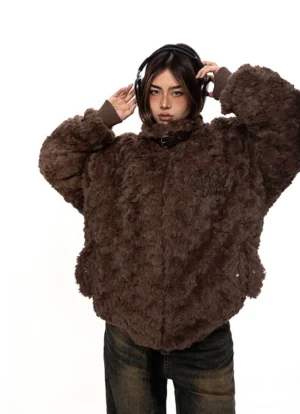 Close-up view of brown fuzzy fleece oversized coat showing hidden front zipper, buckle neckline detail, embroidered lettering, metal studs, and curved hem
