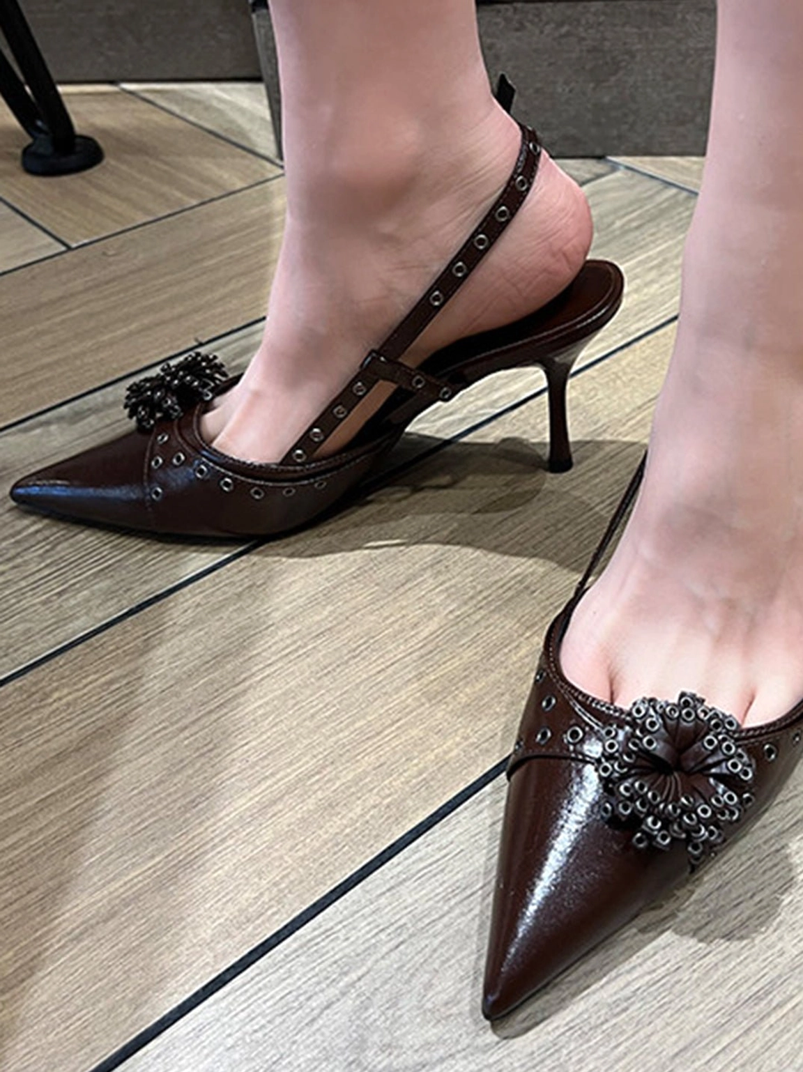 Brown glossy pointed-toe slingback heels shown on feet with beaded floral vamp decoration and studded slingback straps