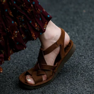 Brown leather fisherman sandals shown from a three-quarter side view with adjustable ankle fastening, open heel, and textured woven upper