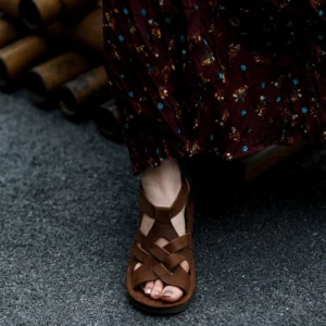 Brown leather fisherman sandals worn with a floral skirt, showing woven crisscross straps, open toe design, matte finish, and thick rubber outsole