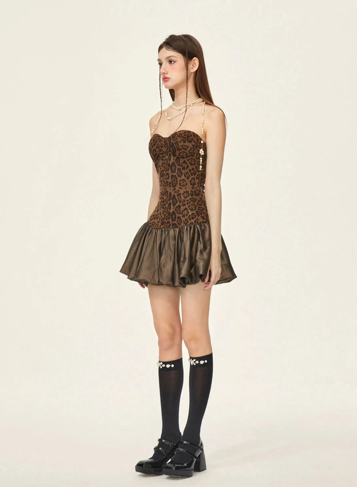Side view of fitted brown leopard print strapless mini dress with pearl chain details knee-high socks and platform shoes