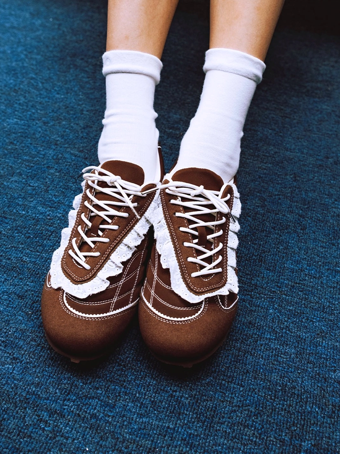 Brown low-top trainer sneakers on feet showing the ruffled lace trim white laces and classic slim streetwear silhouette