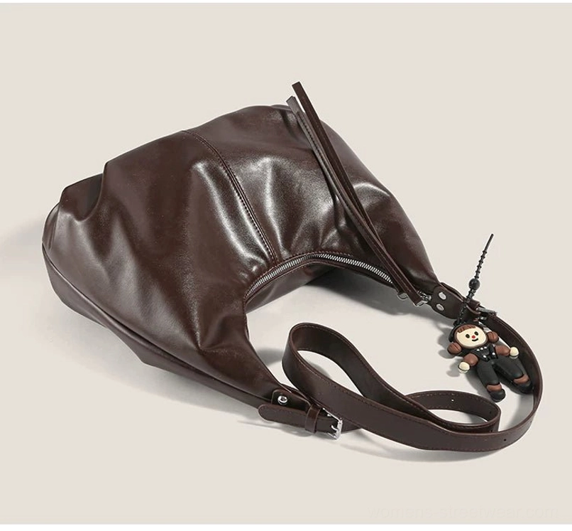 Overhead side view of a brown monkey charm crescent bag displaying the adjustable strap, glossy finish, and dangling pendant