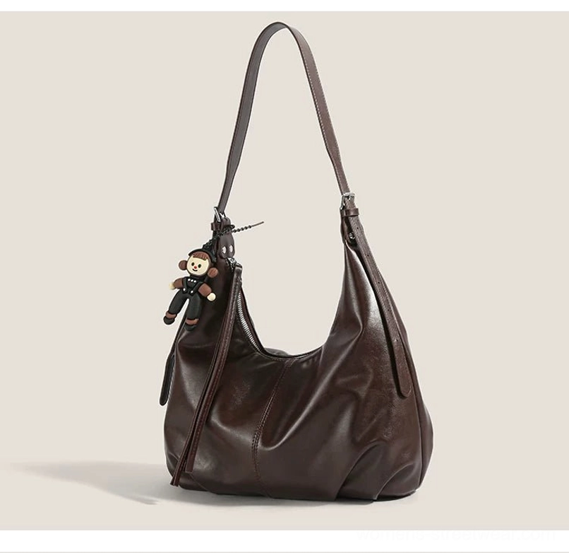 Back three-quarter view of a brown monkey charm shoulder bag showing the leather tassel, curved profile, and dangling pendant