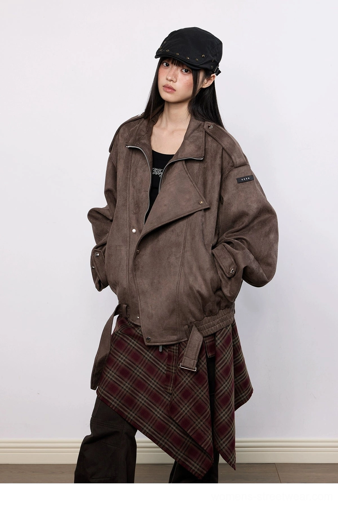 Three-quarter view of a model wearing an oversized brown faux suede biker jacket with plaid skirt cargo trousers and leather handbag