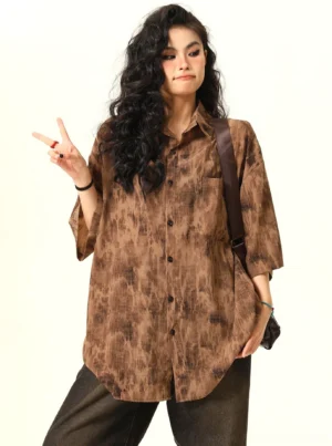Three-quarter view of a brown oversized tie-dye streetwear shirt styled with dark wide-leg jeans and a leather crossbody bag