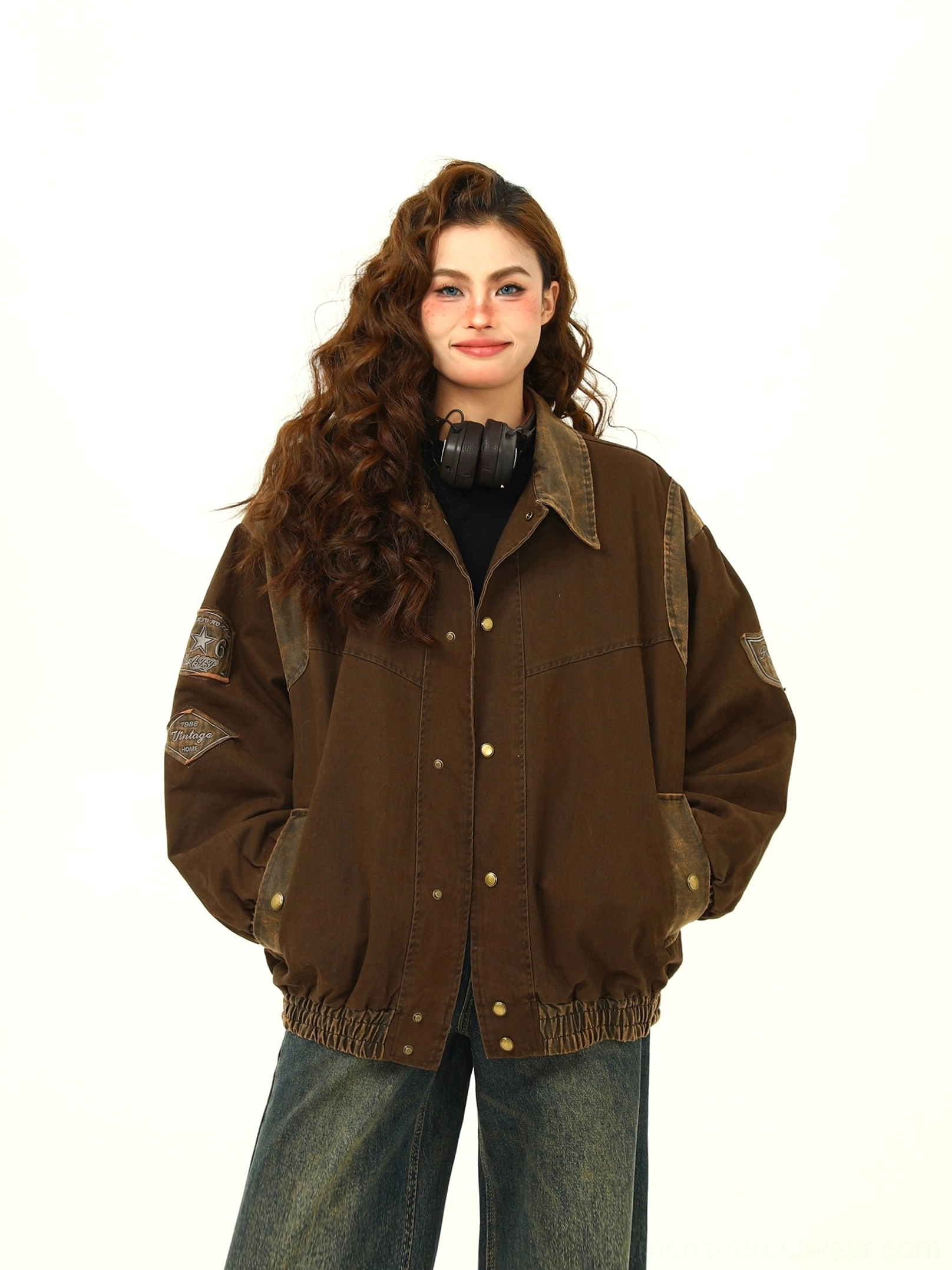 Front detail view of a woman wearing a brown oversized varsity jacket with metal snap-button closure, side pockets, color-block sleeves, and black inner top