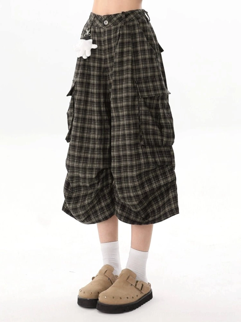 Front low angle view of brown plaid wide-leg cargo culotte shorts with large utility pockets and playful white character plush pendant