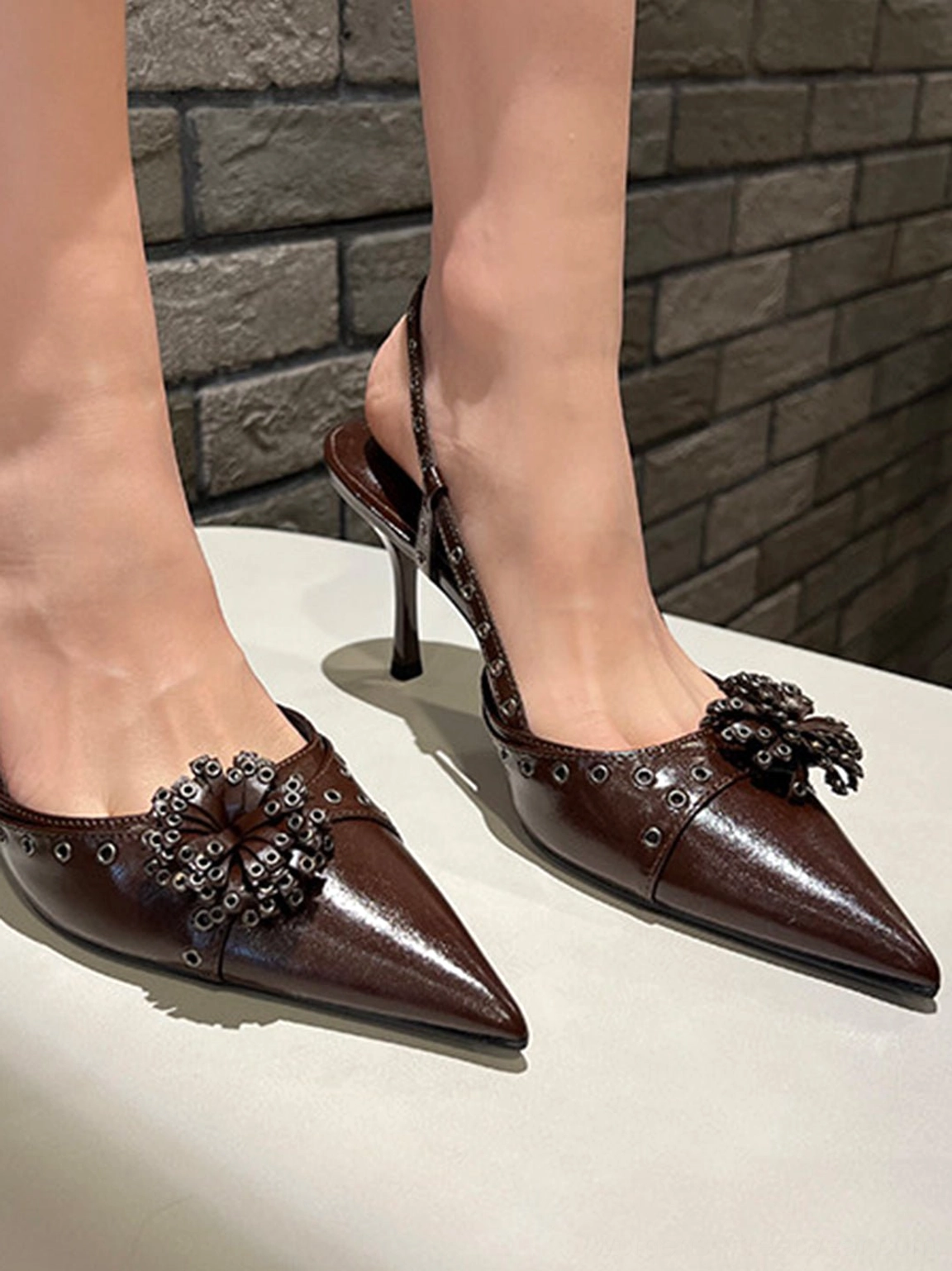 Brown pointed-toe stiletto slingback heels with glossy synthetic upper, floral beaded applique, and decorative rivet straps