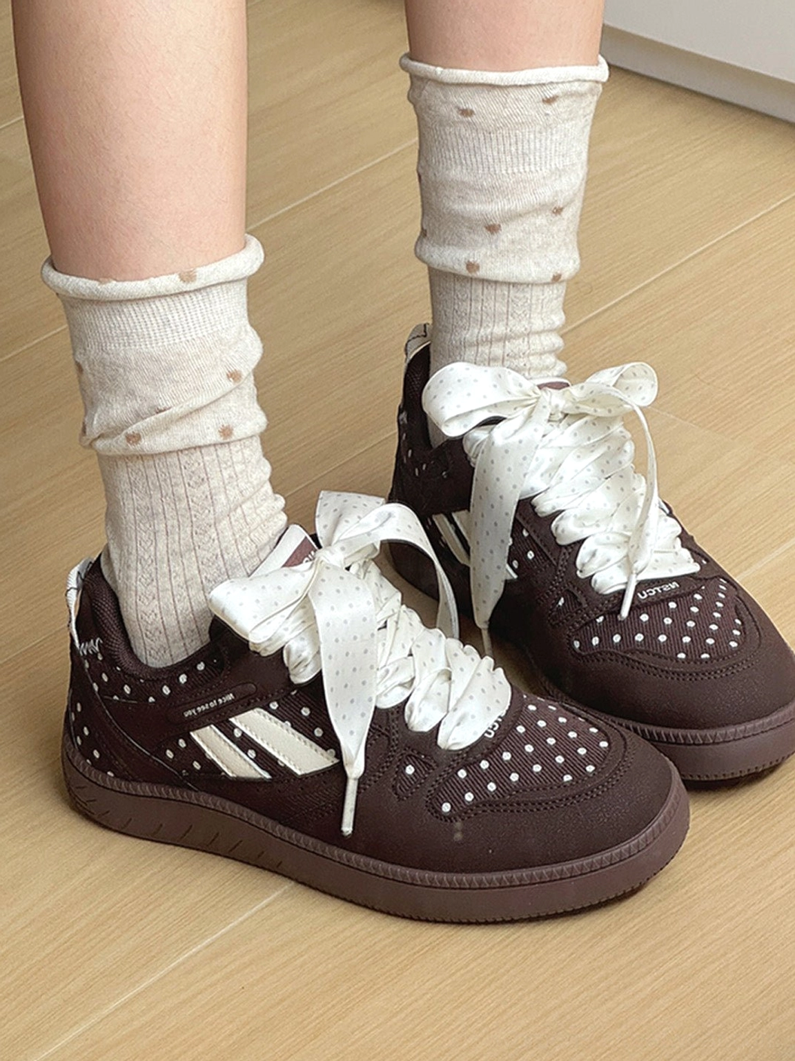 Brown polka dot low top skate sneakers paired with beige dotted socks on a wooden floor