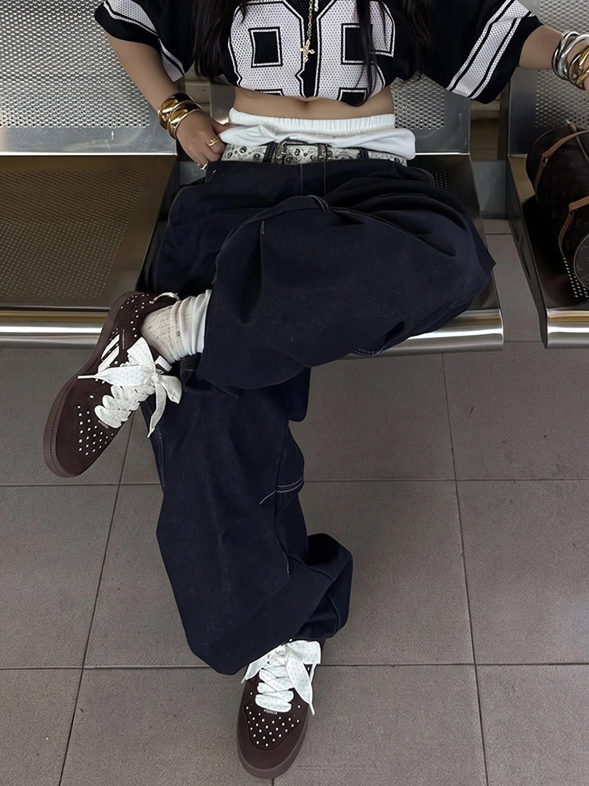 Brown polka dot ribbon sneakers worn on crossed feet with a casual Korean-inspired streetwear outfit