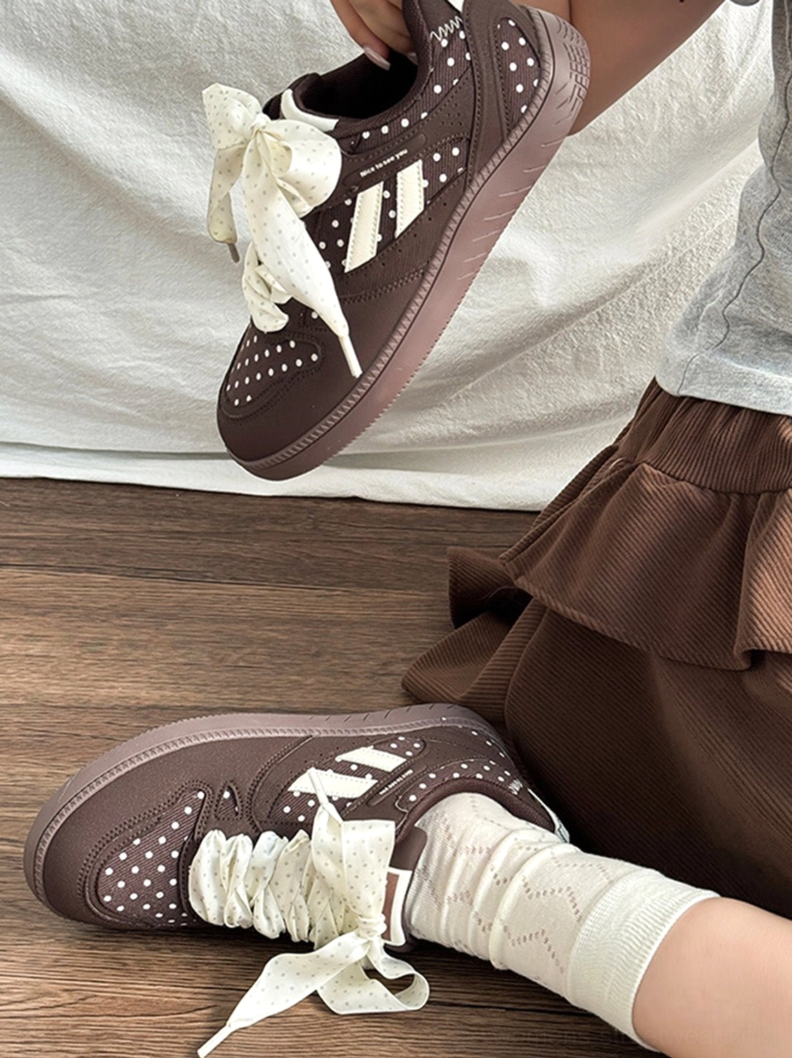 Angled close-up of brown polka dot ribbon sneakers styled with a ruffled skirt for a playful streetwear outfit