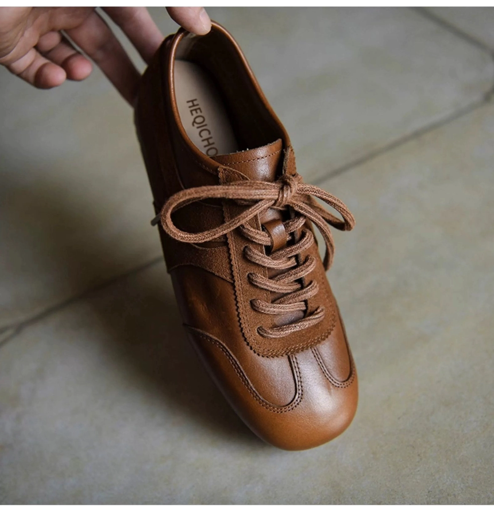 Brown retro leather sneaker held by the heel, showing suede laces, classic low-top profile, mixed-material upper, and cushioned interior