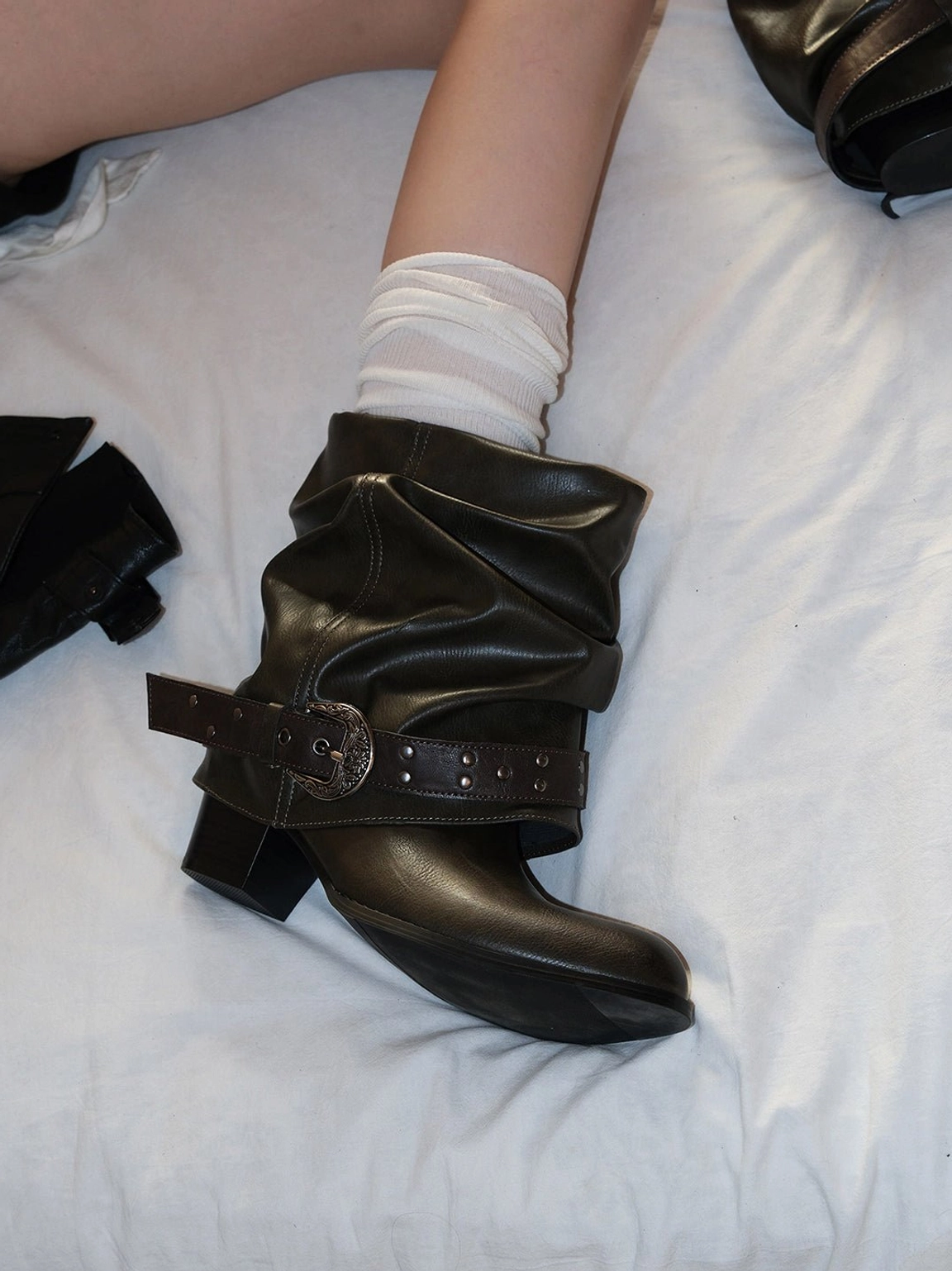 Close-up three-quarter view of brown slouchy cowhide ankle boots with a decorative western buckle strap and low block heel