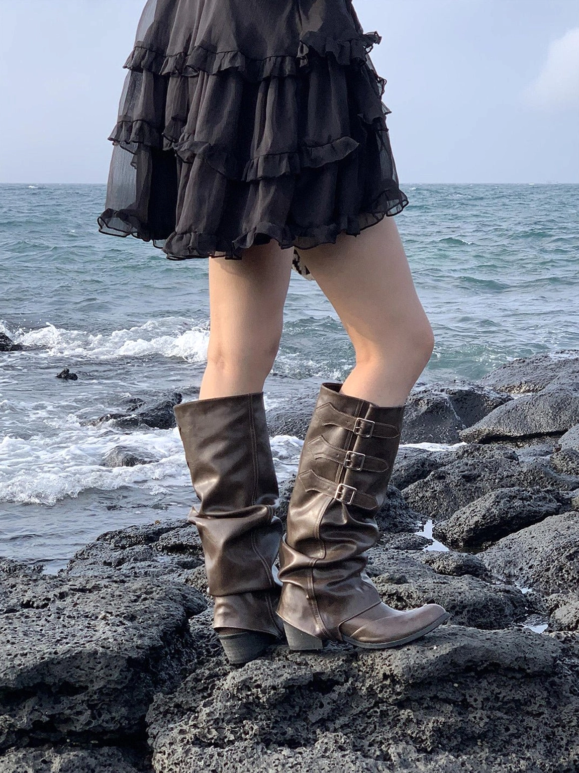 Brown slouchy western knee-high boots with faded finish, pointed toe, and buckle closures styled for streetwear