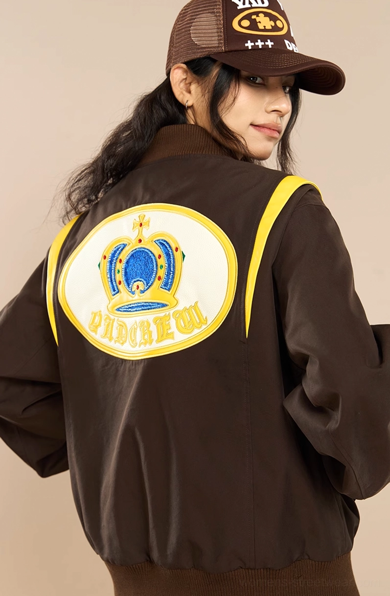 Side profile of brown crown embroidered streetwear baseball jacket with yellow shoulder trim and matte fabric
