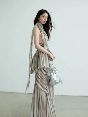 Brown striped halter dress set with long halter sash, layered ruched waist, and flowing maxi skirt shown from the side with a silver shoulder bag