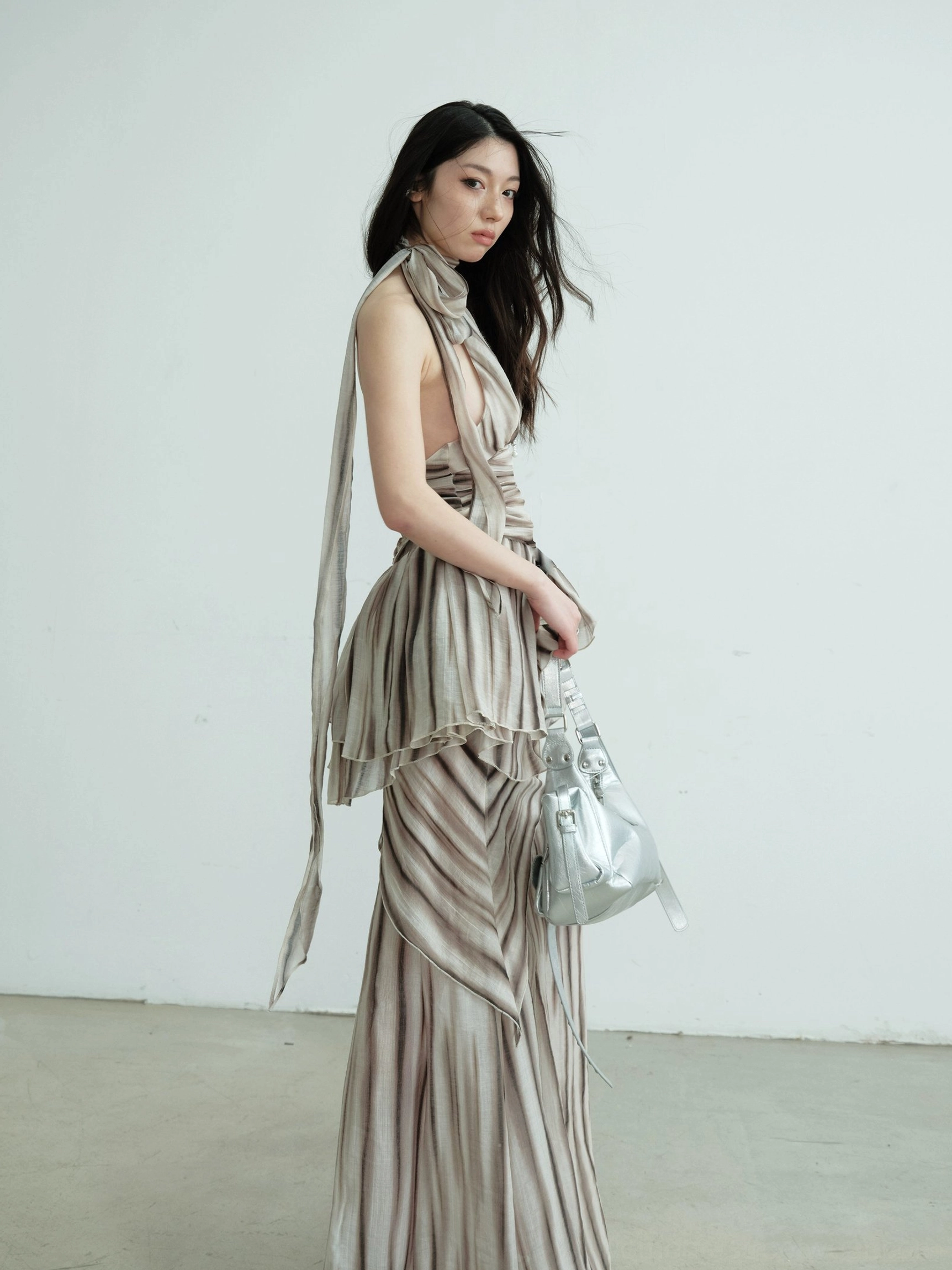 Brown striped halter dress set with long halter sash, layered ruched waist, and flowing maxi skirt shown from the side with a silver shoulder bag