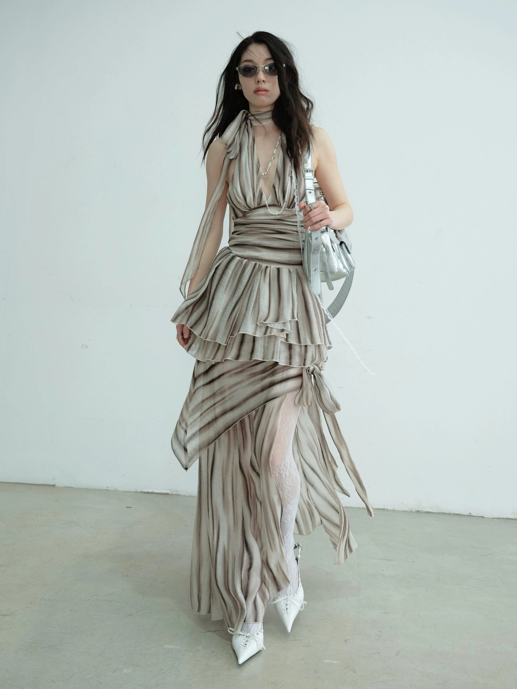 Front three-quarter view of brown striped halter two-piece dress with ruched ruffled waist, high side split, draped skirt panels, and silver handbag
