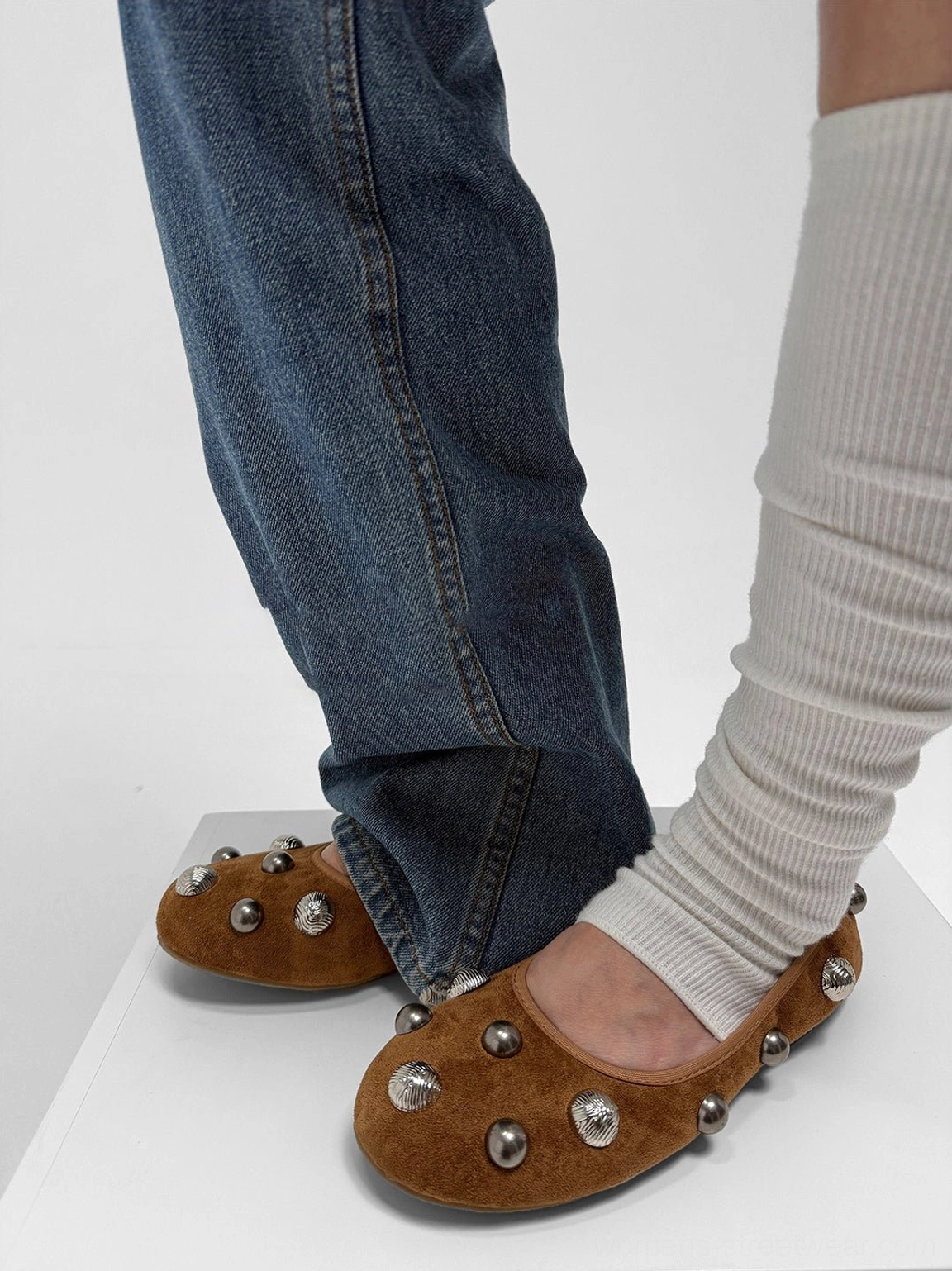 Side view of brown studded ballet flats worn with blue denim and white ribbed socks, highlighting the embellished outer side