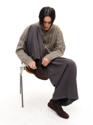 Brown suede minimalist lace-up sneakers worn with wide-leg grey trousers and a neutral knit sweater in a modern studio outfit