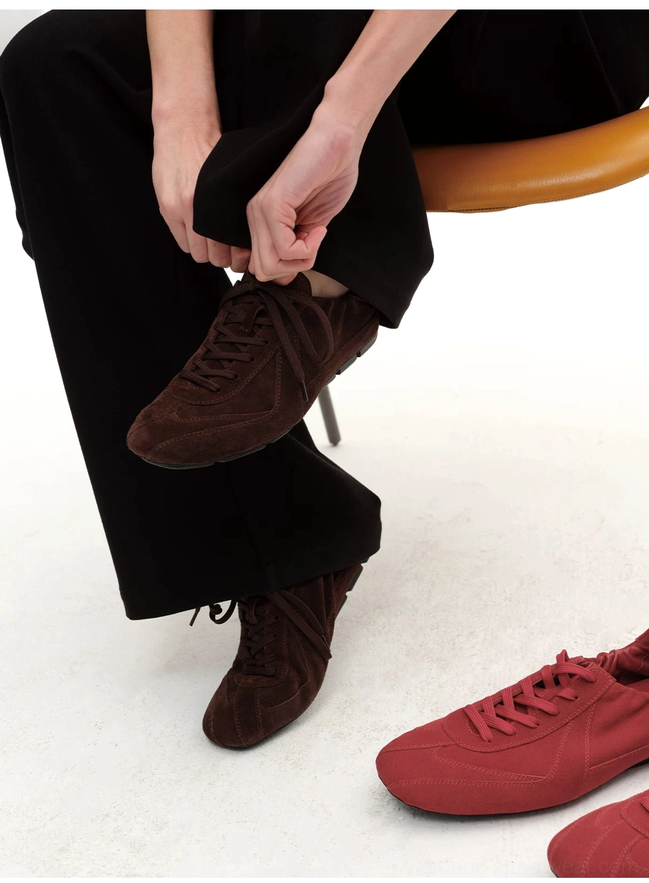 Brown suede minimalist low-top lace-up sneakers being worn with black trousers in a clean modern studio setting