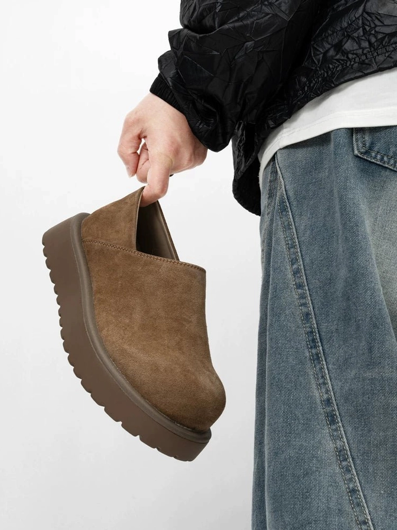 Brown suede-look platform slip-on clogs held in hand with blue jeans and urban streetwear styling