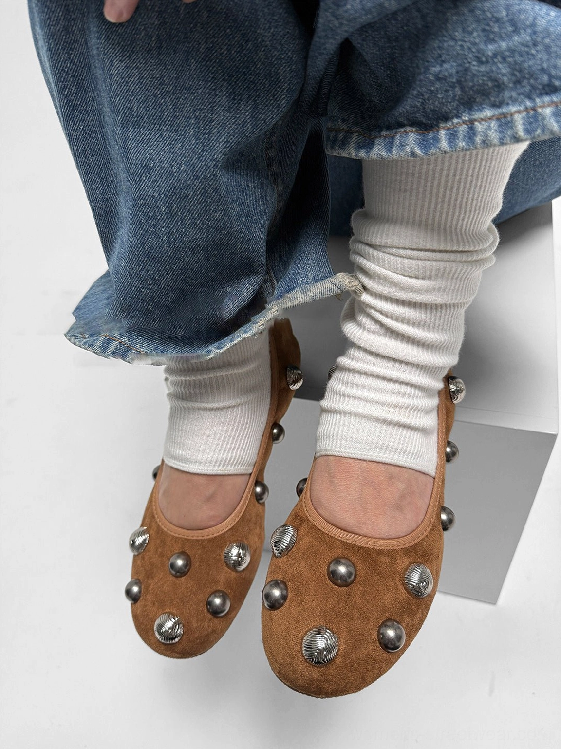 Close-up top view of brown suede-look studded ballet flats worn with blue jeans and white ribbed socks