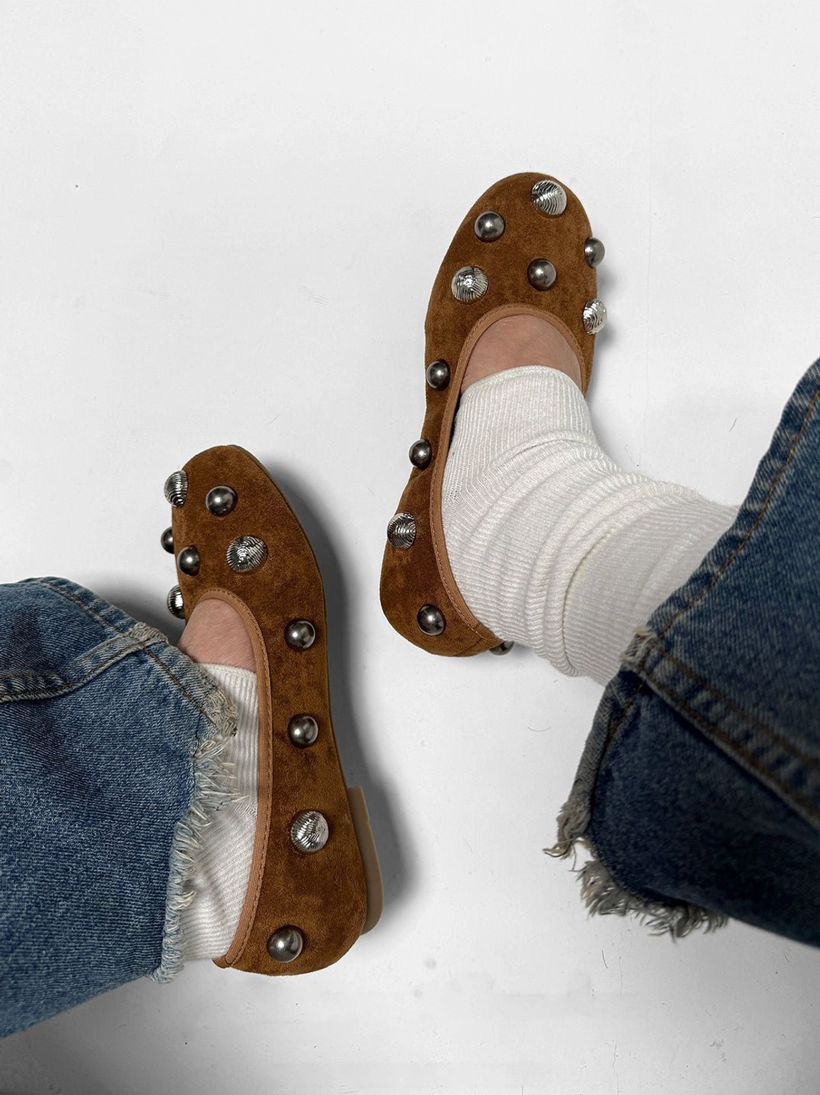 Rear-side view of brown suede-look studded ballet flats with white ribbed socks and blue denim styling
