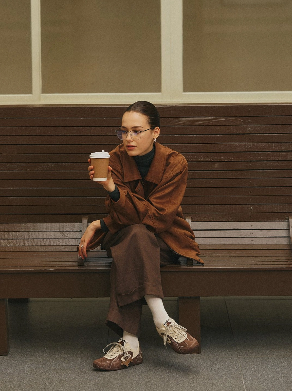 Brown swirl panel retro trainers styled with a full brown casual outfit and white socks in a cafe setting