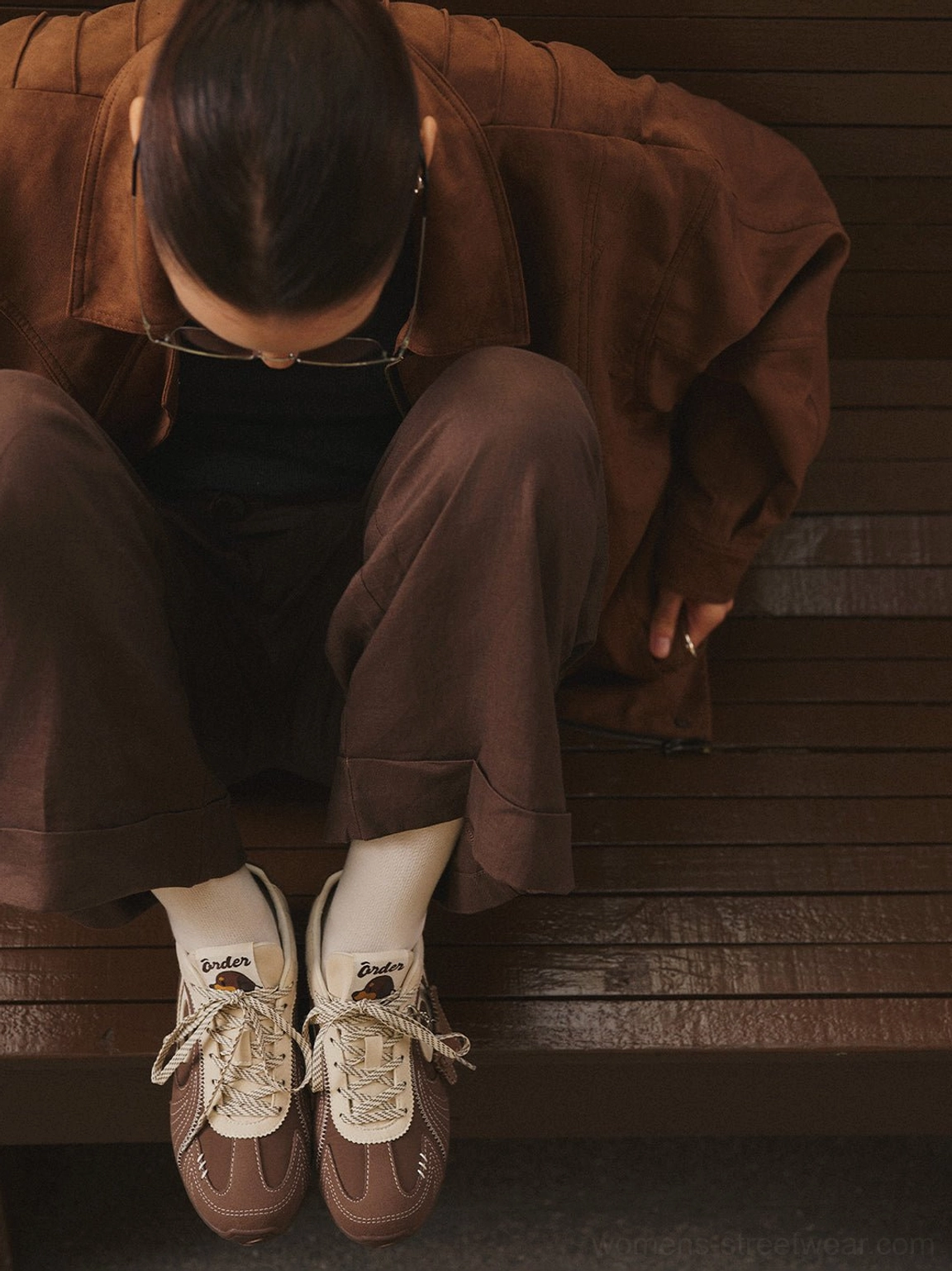 Close-up of brown swirl panel retro trainers worn with white socks and a tonal brown casual outfit