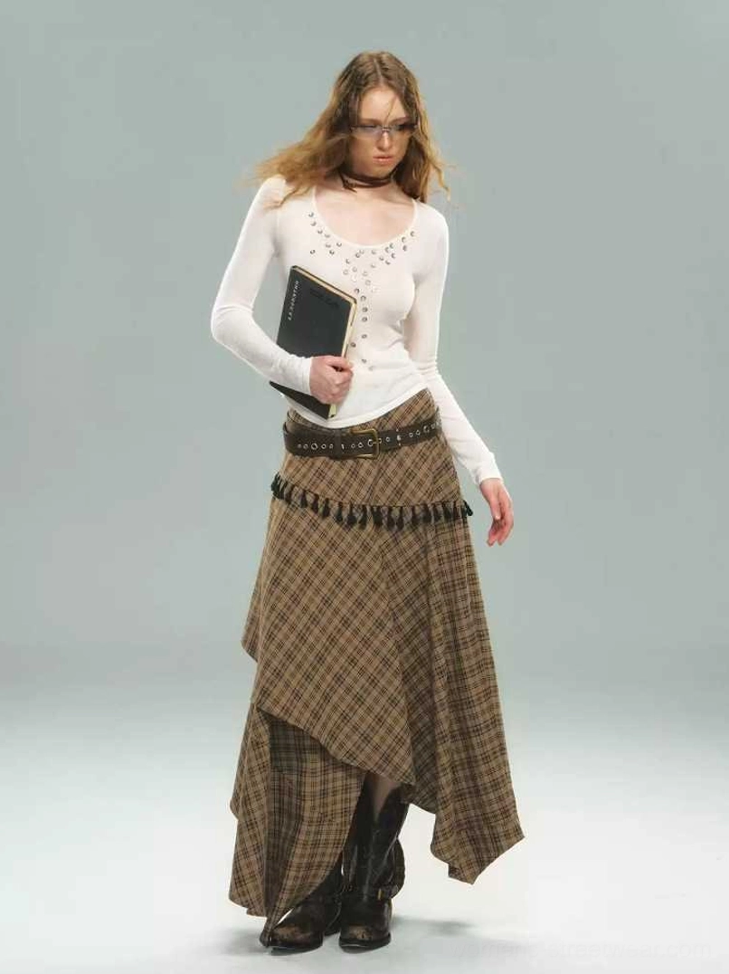 Model wearing a brown tartan asymmetric tassel skirt with layered uneven hem, black tassel trim, and white long sleeve top in a streetwear studio outfit