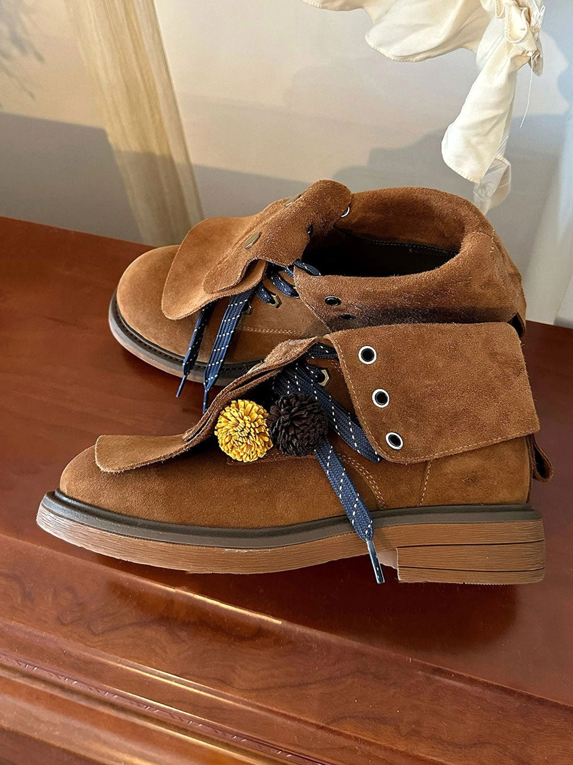 Pair of brown tassel-flap suede-look ankle boots displayed from above with blue striped braided laces and pom-pom decorations