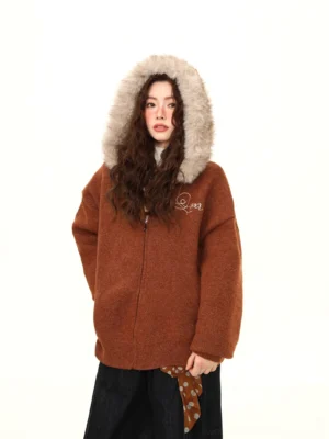 Close front view of a brown streetwear teddy jacket showing the plush faux-fur hood trim, metal zipper, and chest embroidery