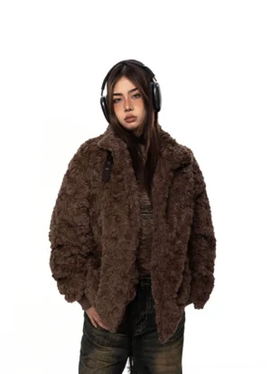 Front view of a woman wearing a brown textured fleece oversized coat with buckle-tab neckline, ribbed cuffs, wide-leg jeans, and black headphones in a minimalist studio