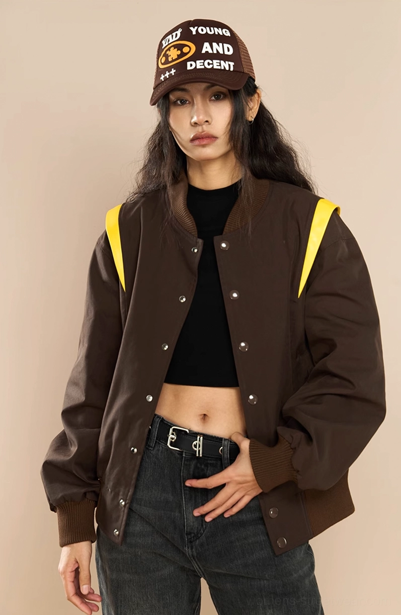 Female model styling a brown crown embroidered varsity jacket with crop top high waisted jeans and trucker hat