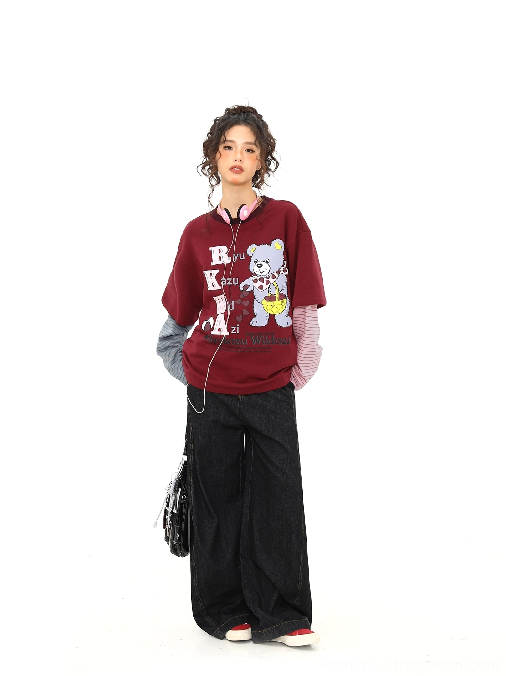 Full-body side view of a woman wearing a burgundy bear print layered streetwear tee with black wide-leg pants and crossbody bag