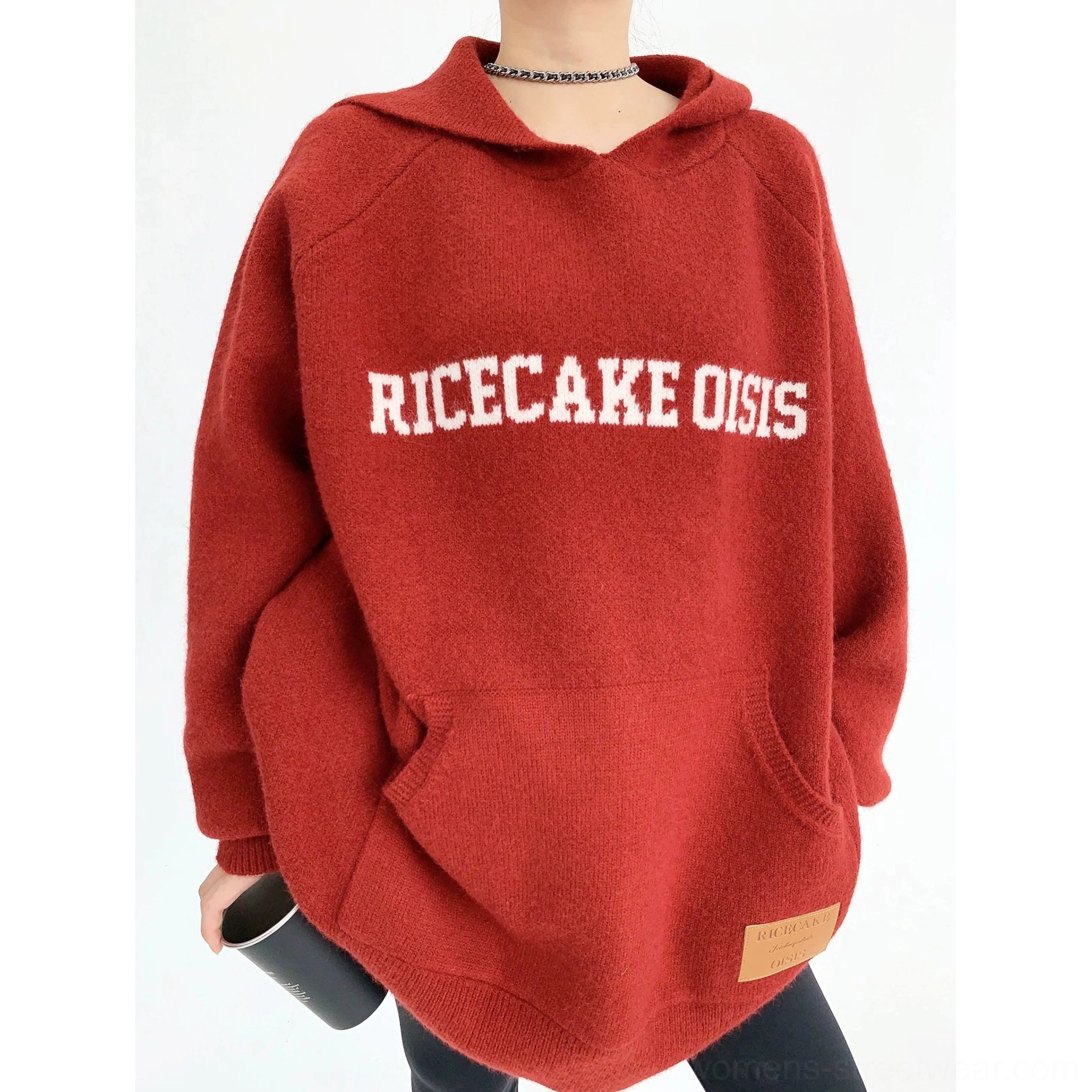 Close-up of burgundy oversized knit hoodie with white RICE CAKE OISHI chest lettering, kangaroo pocket, and faux-leather hem tag