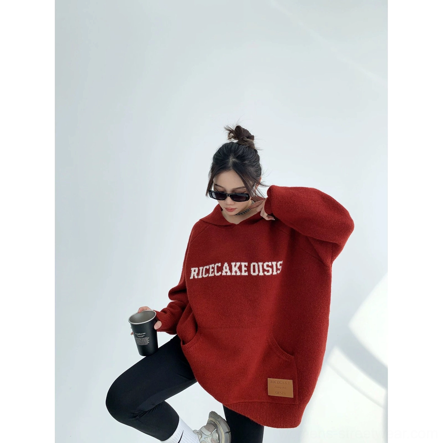 Burgundy oversized knit hoodie shown from the side with long sleeves, relaxed fit, contrast chest lettering, and leather hem patch