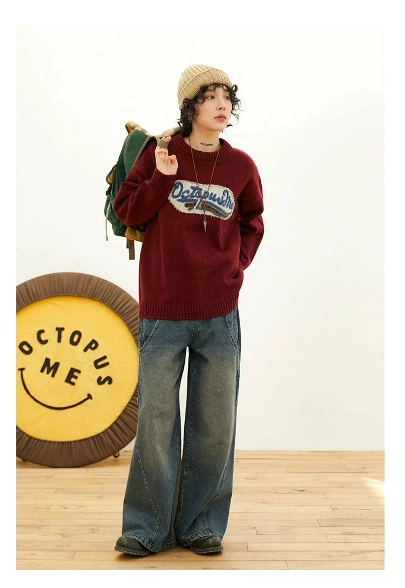 Full-body front view of burgundy oversized vintage knit sweater with textured embroidered patch, beanie, green backpack, and washed denim