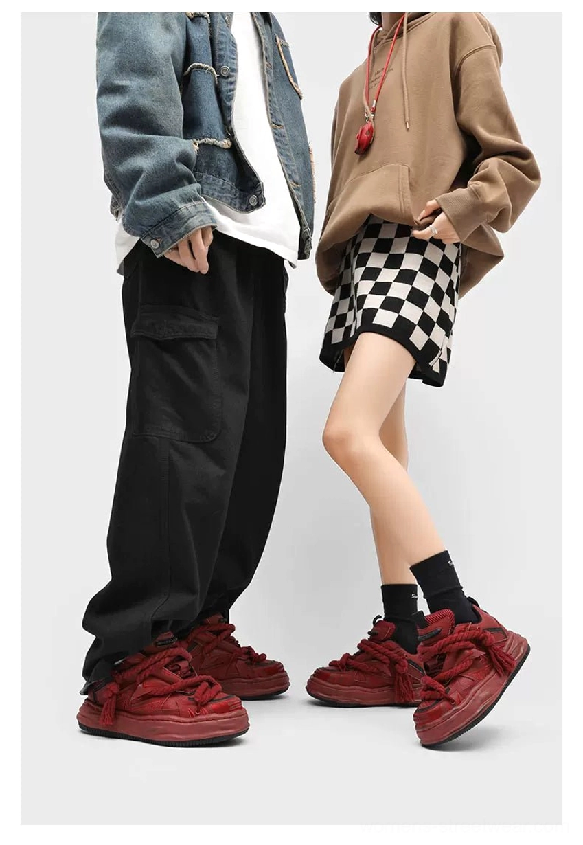 Burgundy red distressed chunky sneakers worn by two streetwear models, featuring oversized braided rope laces, thick distressed soles, and a bold expressive colorway