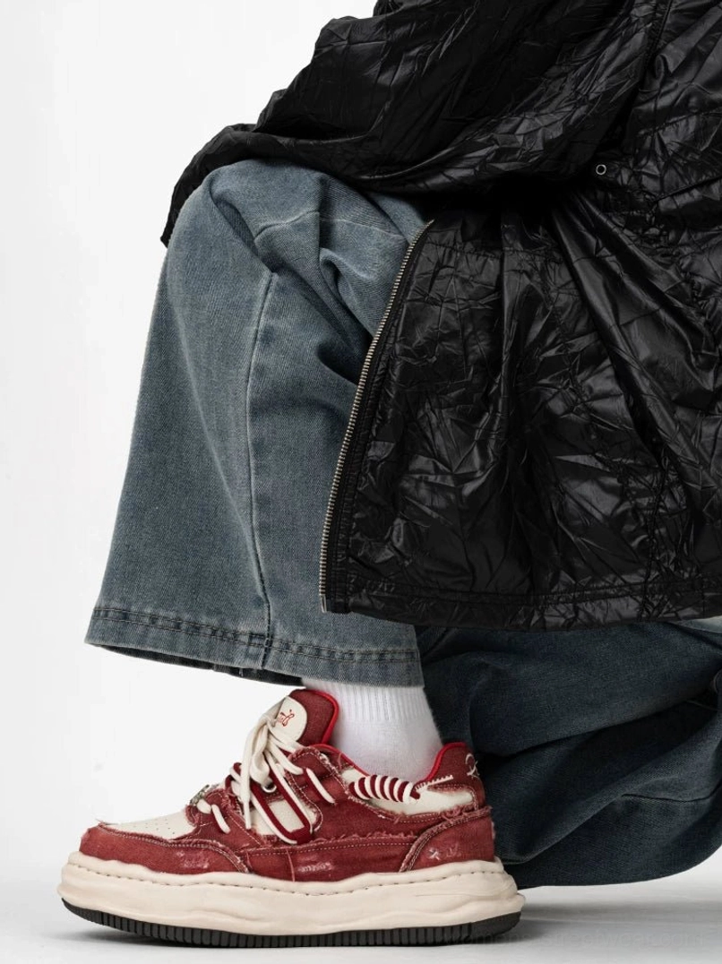 Burgundy red and off white distressed platform sneakers worn with white crew socks and baggy jeans in a modern streetwear outfit
