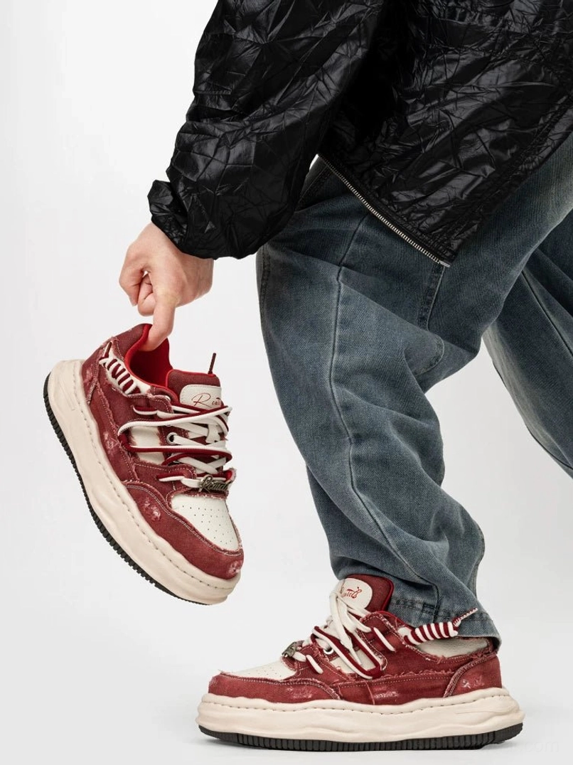 Burgundy red and off white distressed streetwear sneakers with chunky cream platform sole shown from a low side angle with baggy blue jeans