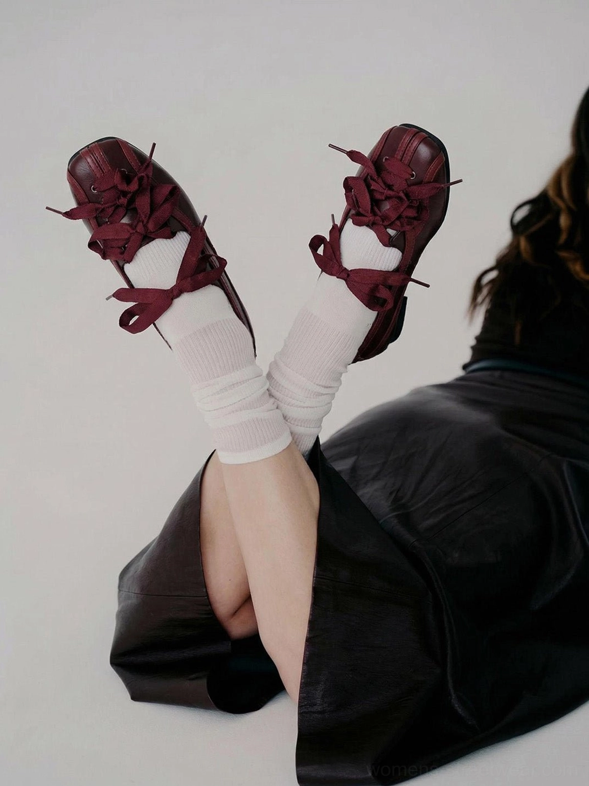 Close-up of burgundy ribbon lace-up ballet flats worn with white crew socks and a black leather skirt
