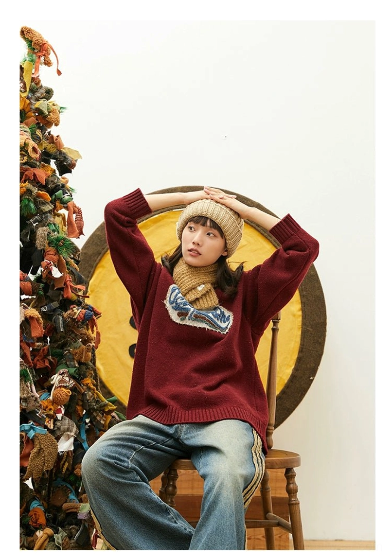 Front view of burgundy speckled oversized knit sweater with dimensional embroidered patch, beige beanie, scarf, and retro winter styling