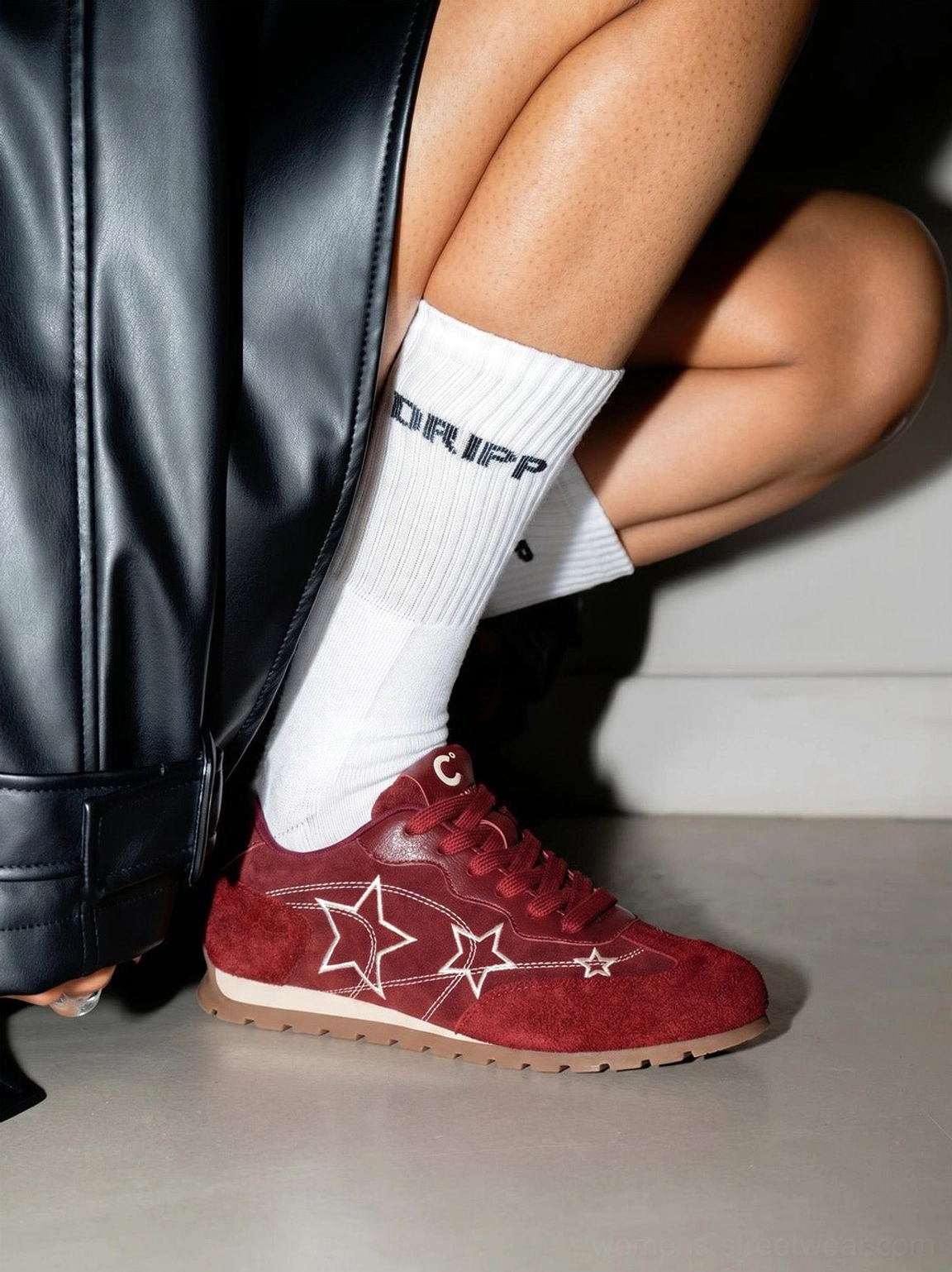 Burgundy star embroidered low-top sneakers worn with printed white crew socks and black leather streetwear outfit