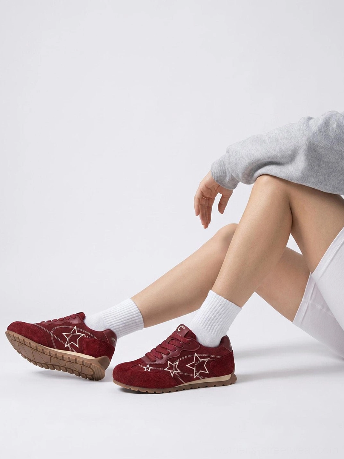 Pair of burgundy star embroidered retro sneakers worn with white socks biker shorts and grey sweatshirt
