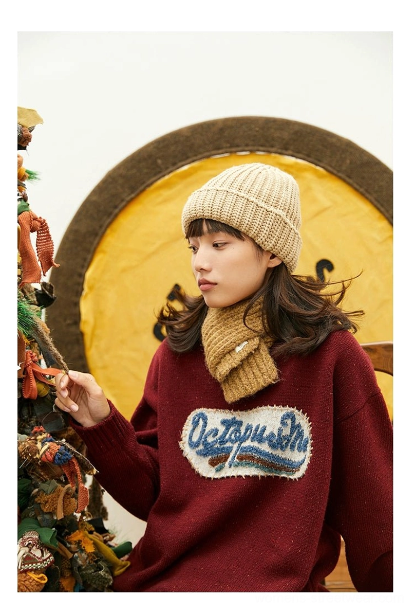 Close-up of burgundy vintage knit sweater showing soft fuzzy texture, detailed layered embroidered patch, and relaxed crewneck streetwear silhouette
