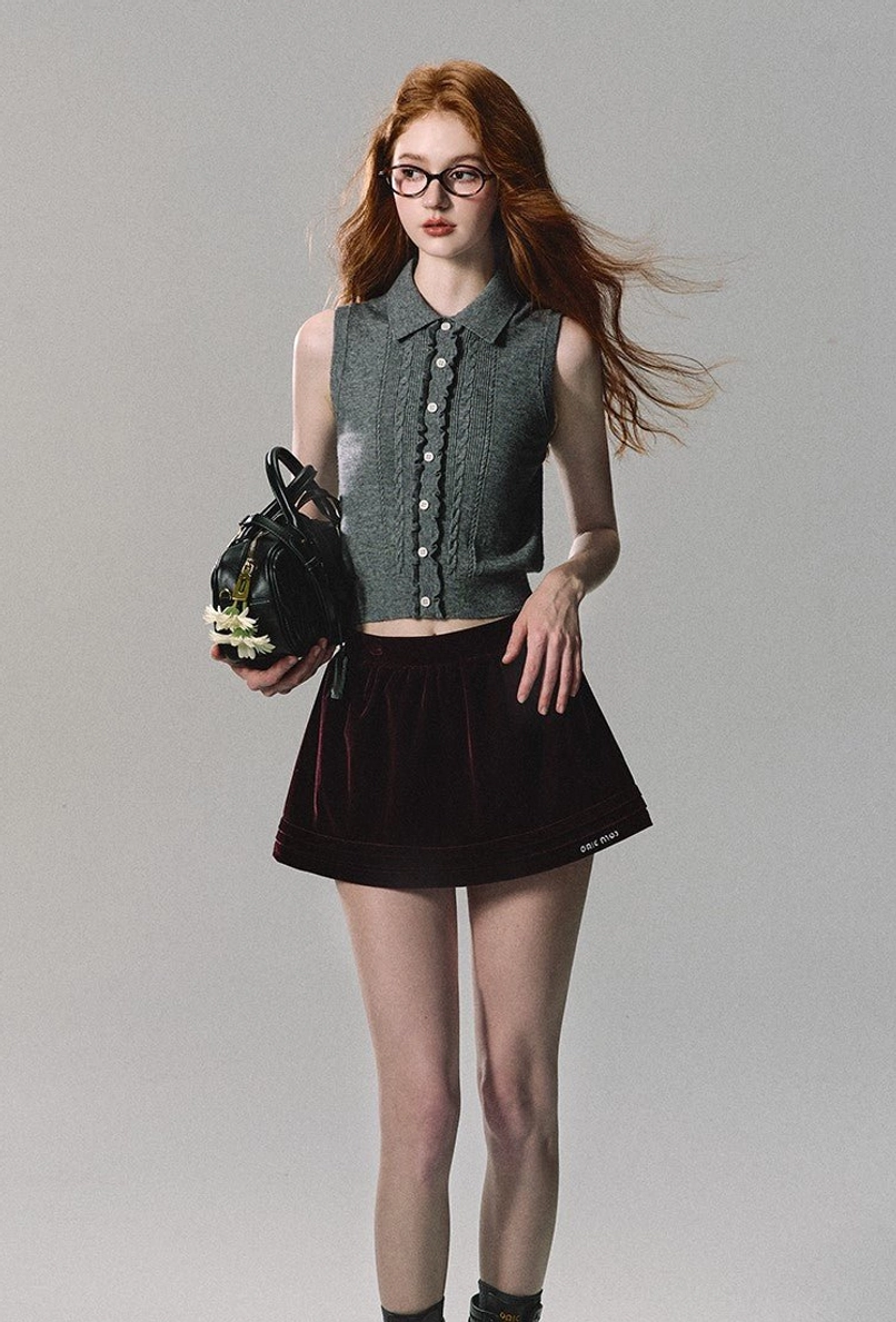 Burgundy velvet A-line mini skirt paired with a fitted cropped button-front knit vest and floral handbag